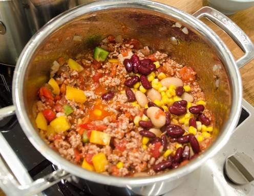 Fügen Sie nun Mais, Tomaten, Paprika und Bohnen hinzu und lassen Sie es solange mit köcheln, bis die