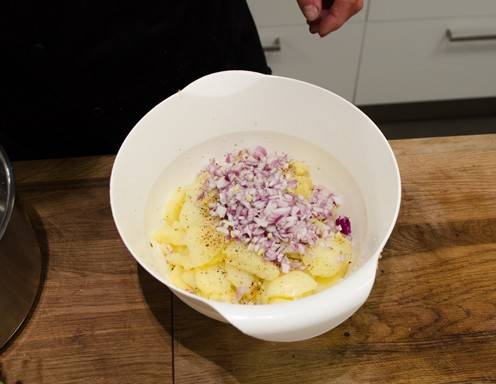 Die Zwiebeln zu dem Kartoffelsalat hinzugeben.